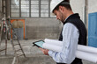 © Veam/Westend61 - Male architect with blueprints using digital tablet while standing in building