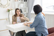 © klavdiyav - two young women conduct a coaching session in home office in light interior with laptop and flowers on tablework with metaphorical cards and psychological counseling