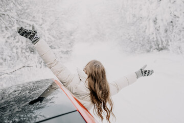 Happy woman looks out of the car window, spreading her arms in different directions. Winter forest.