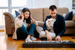 © Jake Jakab/ADDICTIVE STOCK - Man playing synthesizer and woman listening to music in headphones while sitting on floor at home and recording new song