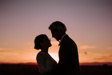 Side View Silhouettes Of Romantic Newlywed Couple Standing Face To Face On Spacious Field Against Purple Sunset Sky
