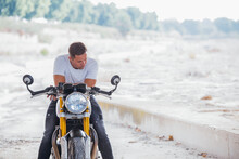 Stylish Male Biker Sitting On Modern Motorcycle In Urban Area And Looking Down