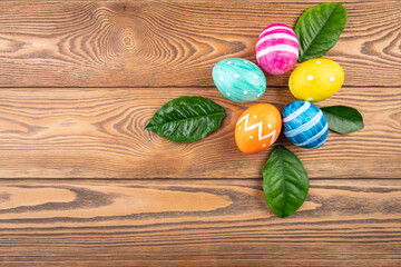 Wall Mural - Cute Easter eggs decorated handmade with paint and paintbrush on a wooden background with green young leaves. Copy space