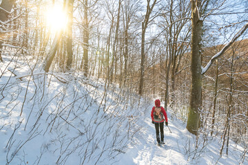 man in outdoor gear with backpack hiking through snowy forest in the winter