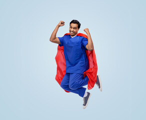 healthcare, profession and medicine concept - happy smiling indian doctor or male nurse in uniform and red superhero cape jumping and celebrating victory over blue background