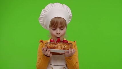 Wall Mural - Portrait of little child girl dressed as cook chef baker blowing up icing sugar from strawberry pie, looking at camera with smile. Kid isolated on chroma key background. Nutrition food, cooking school