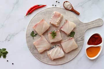 Wall Mural - Uncooked boneless pieces of threadfin fish. Raw Dadha fish cubes placed on a blue plate. clean fish fillets with skin on. Recipe ingredients such as rock salt, coriander, and spices. Copy space.