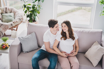 Poster - Portrait of attractive idyllic couple waiting infant sitting on divan spending day daydream time preparing in light house flat indoor