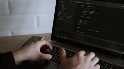 Men's hands press the keys of a laptop keyboard. A man writes a program. The developer is coding. The program code is visible on the screen. Work at home