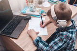 Fototapeta  - A teenage boy following an online lesson in headphones in his bedroom.