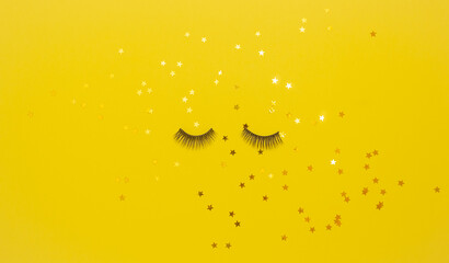 Wall Mural - Artificial eyelashes for makeup on and stars on a yellow background in the center. The concept of eyelash extension. The view from the top.