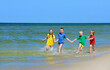 Two girls and two boys in colorful t-shirts running on sandy beach