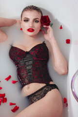 Beautiful young girl in a milk bath with flower petals
holding a red rose. Relaxation concept. Women's Day 8 March.