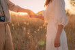 Woman and man holding hands on a golden yellow meadow. There was an orange evening light shining down on both of them in soft tones. Feelings of love and romance. Ideas for Valentine's Day wallpaper.