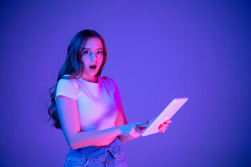 Caucasian woman's portrait isolated on blue studio background in multicolored neon light. Beautiful model with laptop. Concept of human emotions, facial expression, sales, ad, fashion. Copyspace.