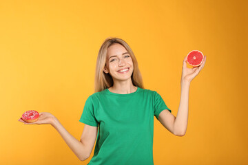 Wall Mural - Woman choosing between doughnut and healthy grapefruit on yellow background