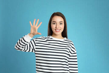 Canvas Print - Woman showing number five with her hand on light blue background