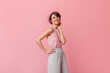 © Look! - Stylish european girl in pants looking at camera. Carefree french lady standing on pink background.
