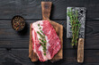 Fresh Raw Round roast beef meat cut on a butcher cutting board with cleaver. Black wooden background. Top view