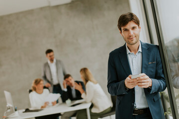 Wall Mural - Handsome young business man standing confident in the office and suing mobile phone