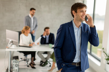 Wall Mural - Handsome young business man standing confident in the office and suing mobile phone