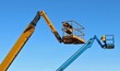 © luca piccini basile - Two cherry picker buckets against blue sky.