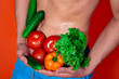 © Denis - A beautiful male body and natural vegetables. Diet and nutrition. Orange background. Broccoli, tomatoes, cucumbers, peppers and lettuce.