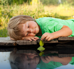 Wall Mural - green leaf-ship in children hand in water, boy in park play with boat in river