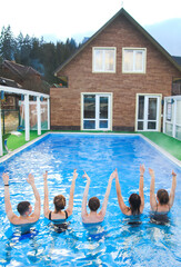 Relax time: group of people from back with raised hands in swimming pool. Relaxation, spa, vacation