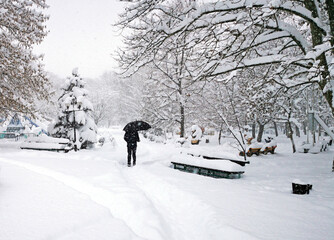 City park and running man with umbrella. Snow-covered trees, bushes and benches in the city park. Russia, Belorechensk, city park in winter.