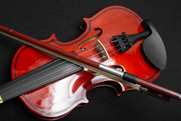 Close view of a classical small violin, strings and bridge over a dark black blanket background
