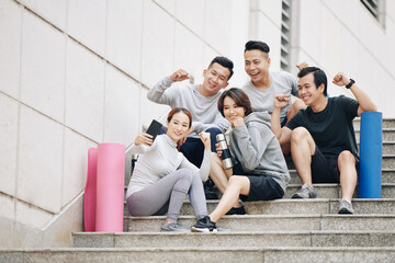 Poster - Happy excited fit friends resting on stairs and doing fist pumps when taking selfie together