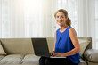 © DragonImages - Portrait of beautiful elegant mature woman sitting on sofa at home and working on laptop