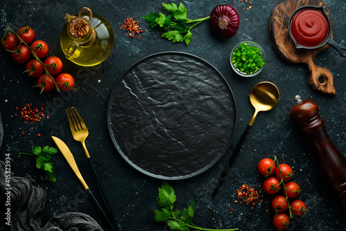 Vegetables, spices and herbs on a black stone background. Kitchen background. Top view. Free space for text. © Yaruniv-Studio