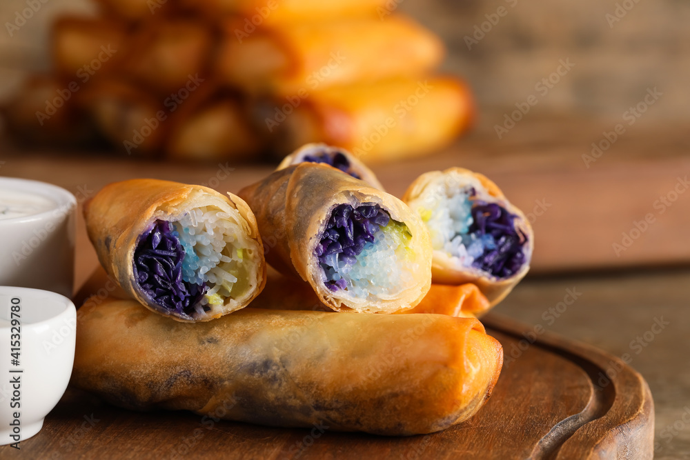 Board with tasty fried spring rolls and sauce on wooden background