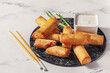 Plate with tasty fried spring rolls and sauce on light background