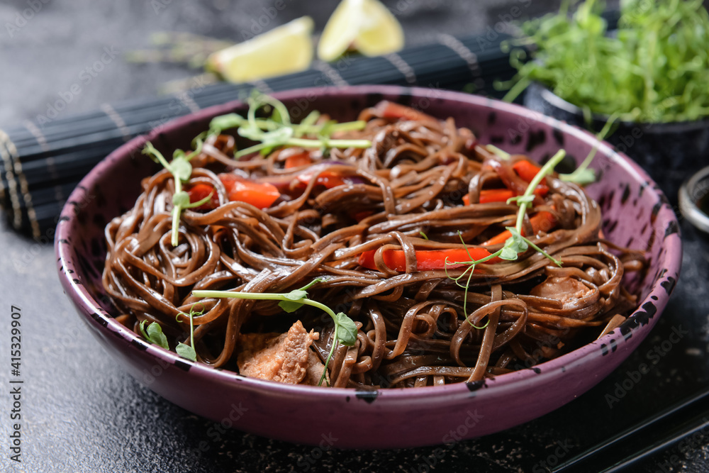 Plate with tasty soba noodles and meat on dark background