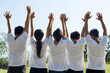 © DragonImages - Happy excited young people in white t-shirts raising arms when standing in city park, view from the back