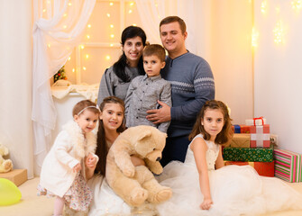 family portrait - parents and children in home interior decorated with holiday lights and gifts