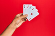 © Krakenimages.com - Hand of hispanic man holding poker cards over isolated red background.