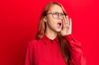 © Krakenimages.com - Young beautiful redhead woman wearing casual clothes and glasses over red background shouting and screaming loud to side with hand on mouth. communication concept.