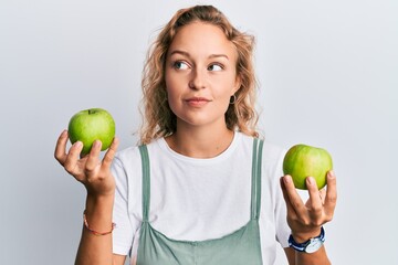 Wall Mural - Beautiful caucasian woman holding green apples smiling looking to the side and staring away thinking.