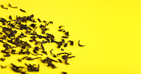 Wall Mural - Dry black loose tea leaves on yellow board, closeup detail from above, space for text right side