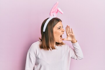 Canvas Print - Young beautiful woman wearing cute easter bunny ears shouting and screaming loud to side with hand on mouth. communication concept.