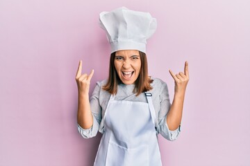 Poster - Young beautiful woman wearing professional cook uniform and hat shouting with crazy expression doing rock symbol with hands up. music star. heavy concept.