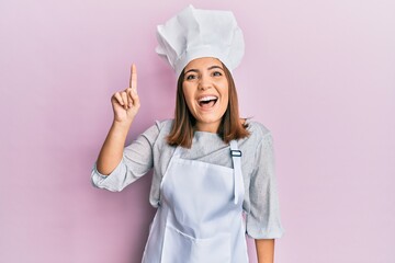 Poster - Young beautiful woman wearing professional cook uniform and hat pointing finger up with successful idea. exited and happy. number one.