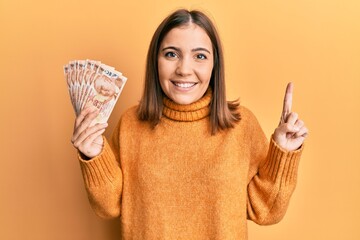 Canvas Print - Young woman holding 50 turkish lira banknotes smiling with an idea or question pointing finger with happy face, number one