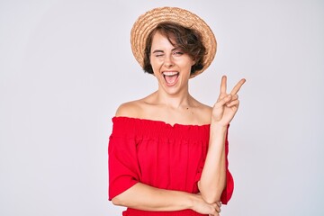 Sticker - Young hispanic woman wearing summer hat smiling with happy face winking at the camera doing victory sign. number two.