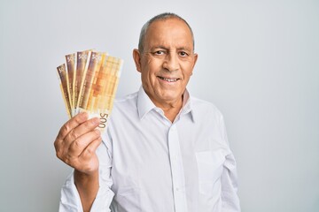 Poster - Handsome senior man holding 500 norwegian krone banknotes looking positive and happy standing and smiling with a confident smile showing teeth