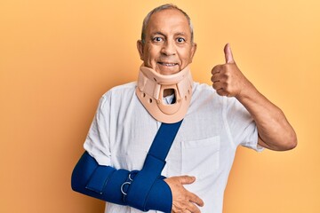 Poster - Handsome mature senior man wearing cervical collar and arm on sling doing happy thumbs up gesture with hand. approving expression looking at the camera showing success.